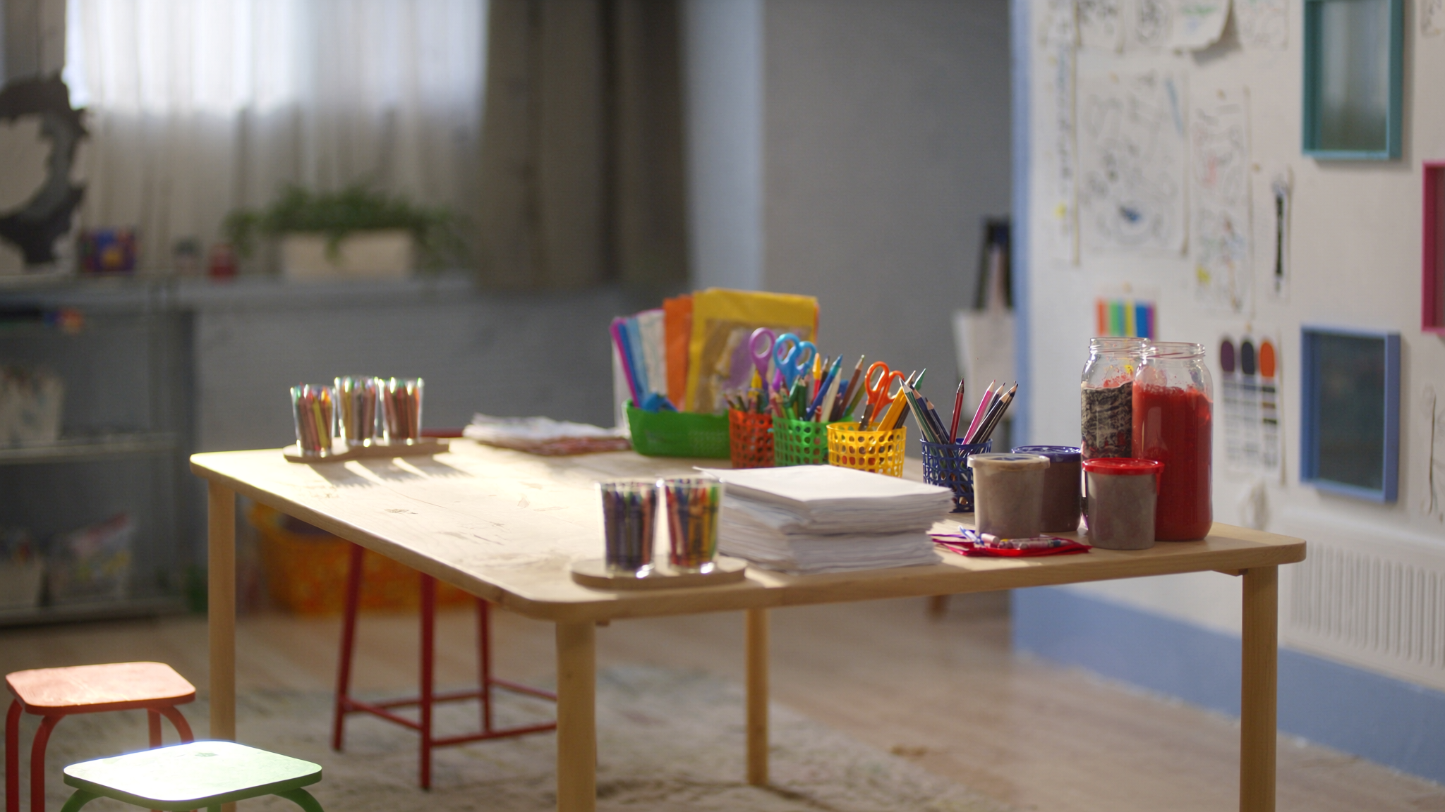 Craft table set with colored pencils, crayons, scissors, paper, and jars of paint