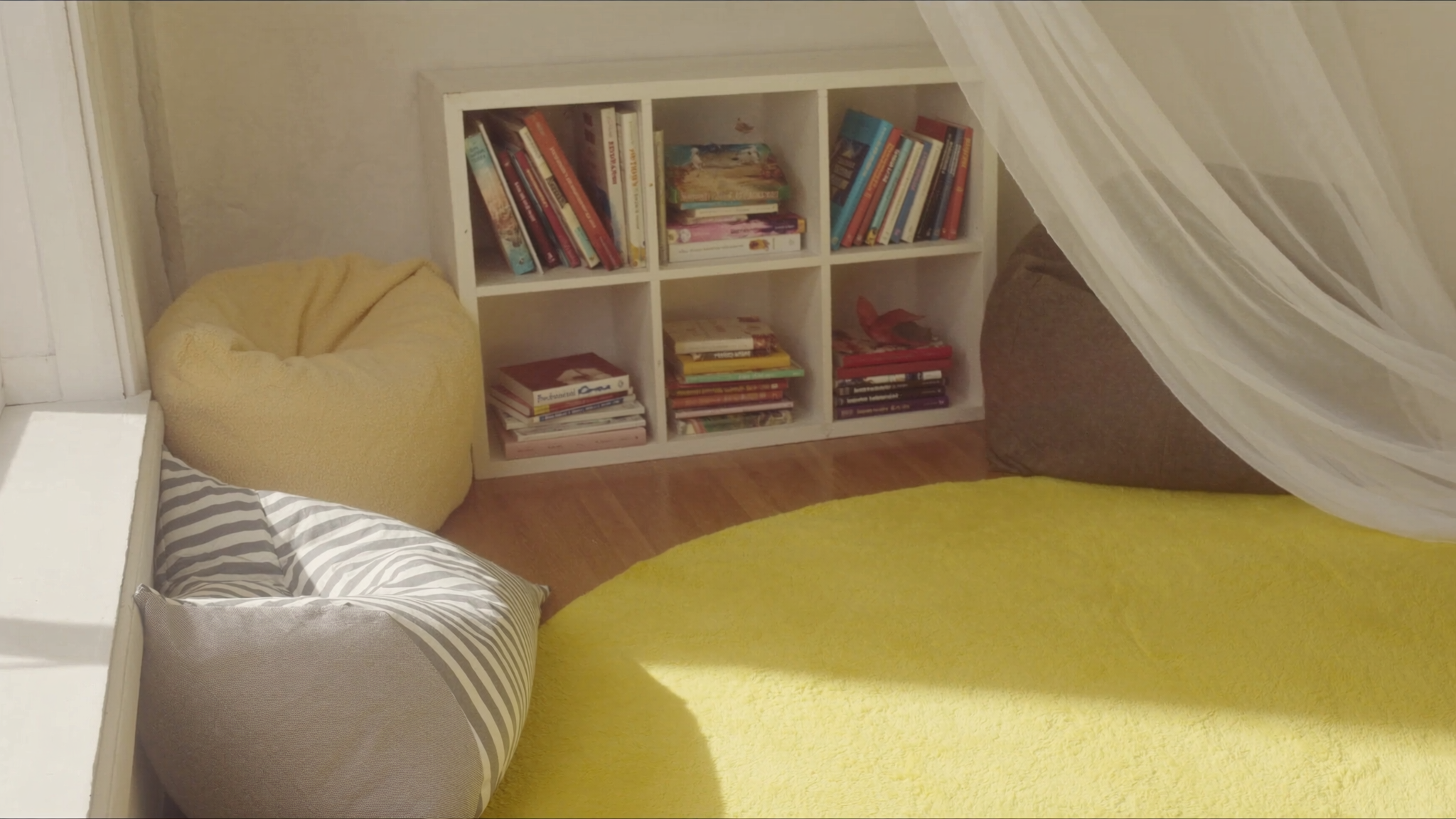 Cozy reading nook with cushioned bean bags, a cube bookshelf of picture books, a soft yellow rug, and a draped canopy