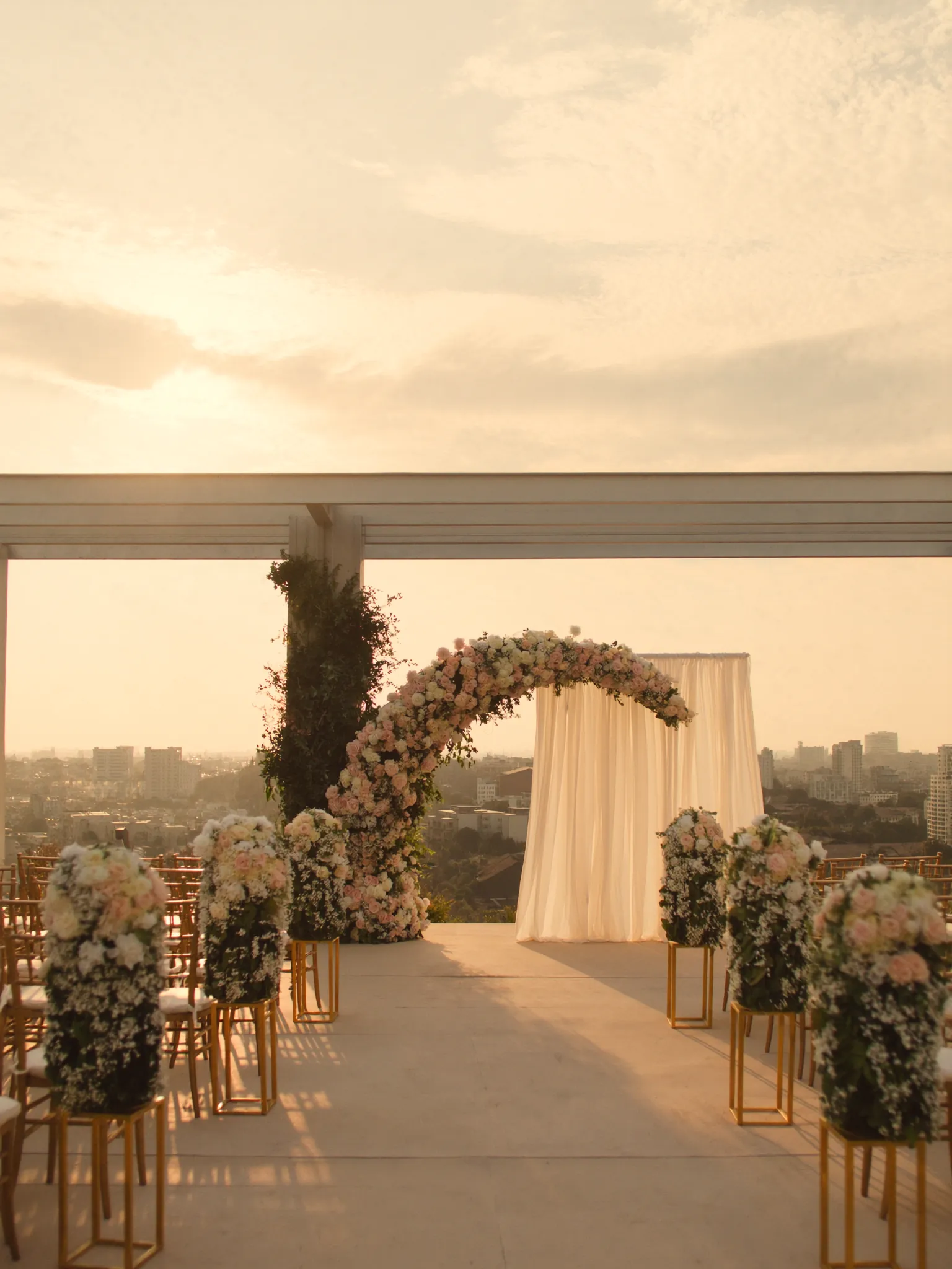 Floral ceremony arch and draped backdrop on the rooftop at sunset