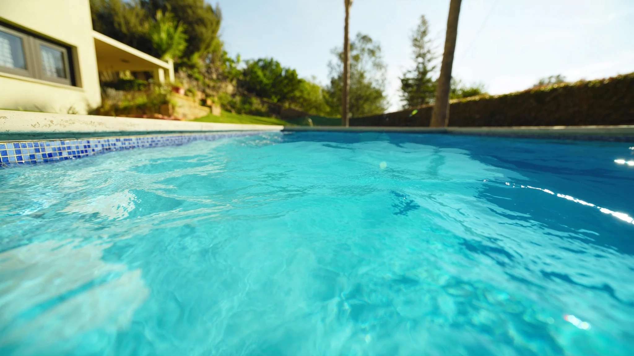 Sunlit residential swimming pool with crystal-clear turquoise water beside a home