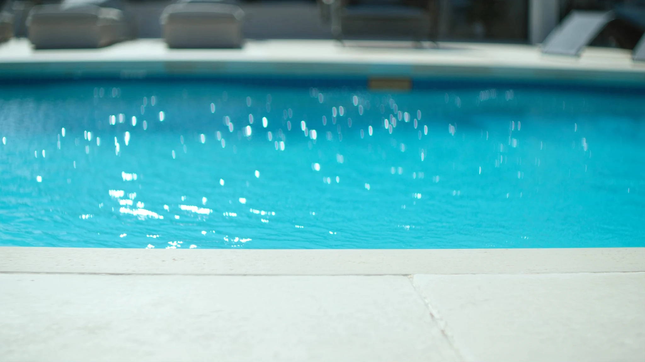 Sparkling pool water beside a clean white deck with loungers in soft focus